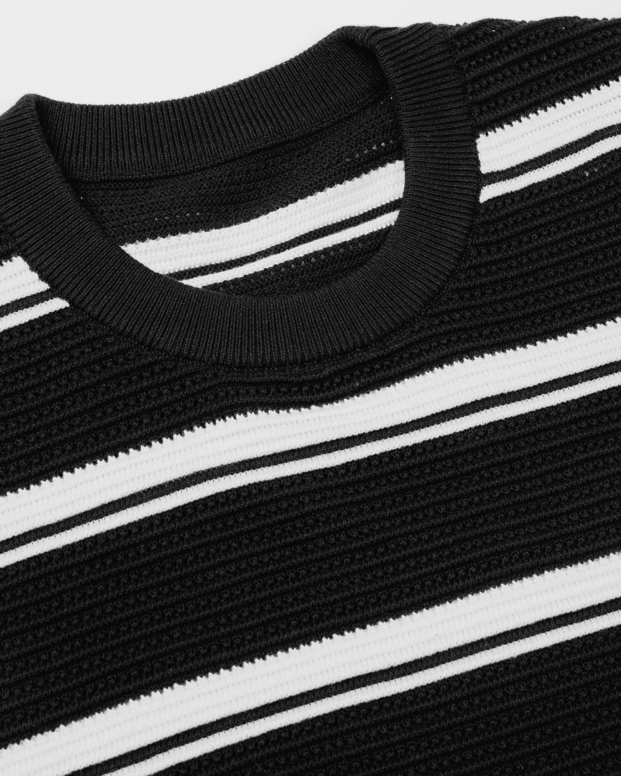 Close-up of a black and white striped ribbed knit crewneck sweater, showing the texture of the knit fabric and collar.