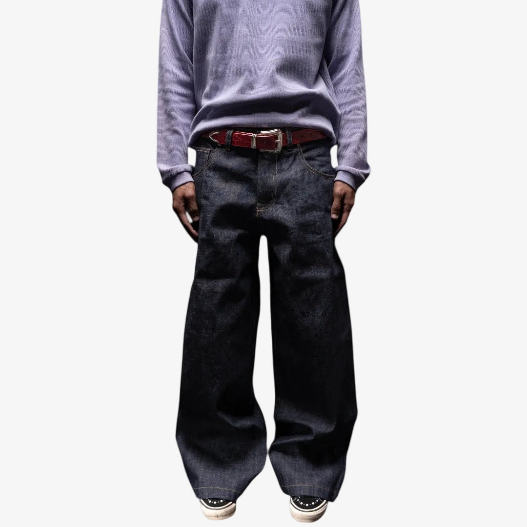 Person wearing a light purple sweater and dark jeans with red croc belt