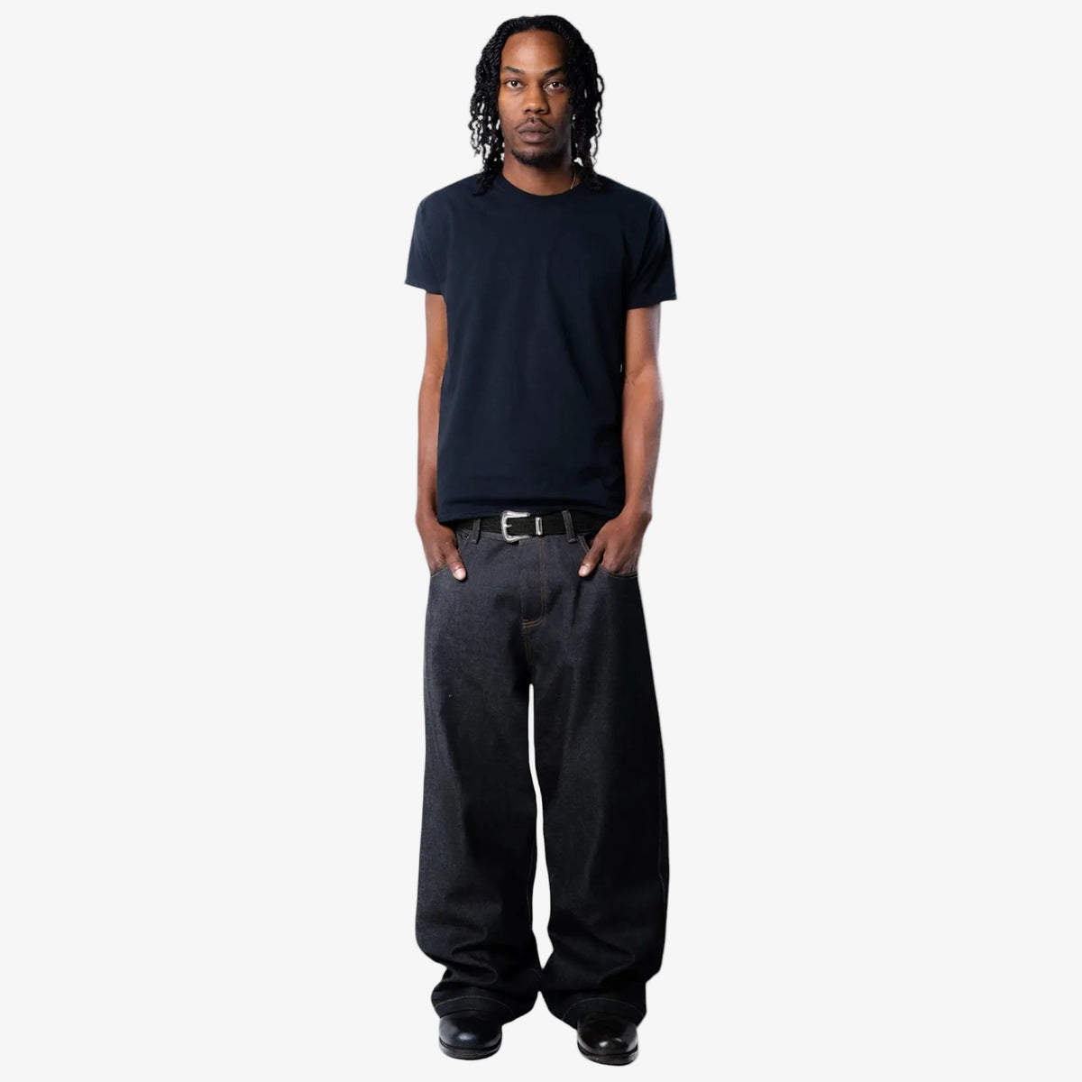 Man wearing a black t-shirt and dark pants with black croc embossed belt on a white background